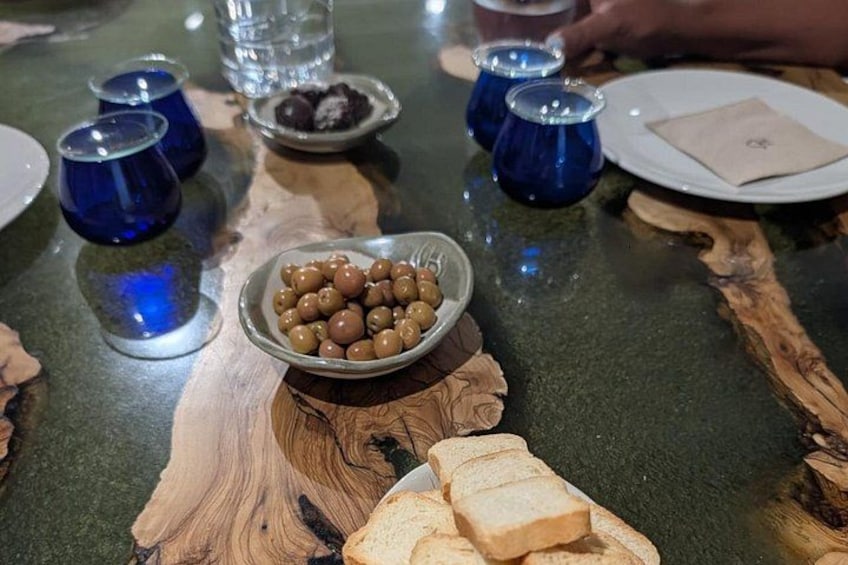 Una mesa con un bol de aperitivos redondos, vasos azules y rebanadas de pan. 3