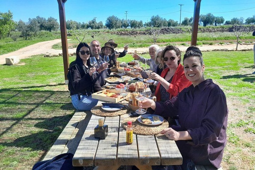 Un grupo de personas disfrutando de un picnic al aire libre, con una mesa de madera dispuesta con comida y bebidas. 4