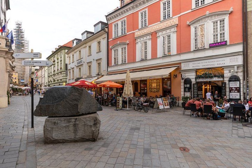 Una piazza lastricata con una grande scultura in pietra, caffè all'aperto ed edifici storici. 5