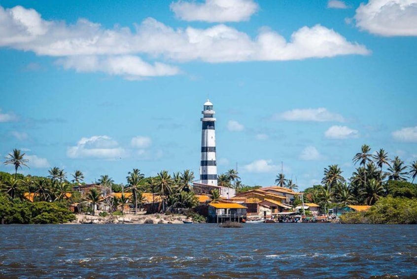 Un faro junto al agua, con palmeras y edificios al fondo. 1