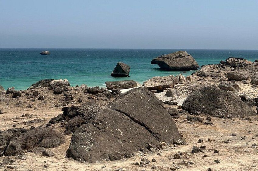 Ein felsiger Strand mit großen Steinen und ruhigem türkisfarbenem Wasser. 5