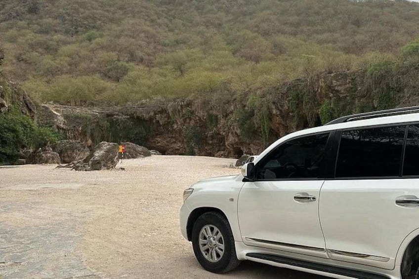 Ein weißer SUV steht auf einem Schotterweg, im Hintergrund eine felsige Hügelkette. 2