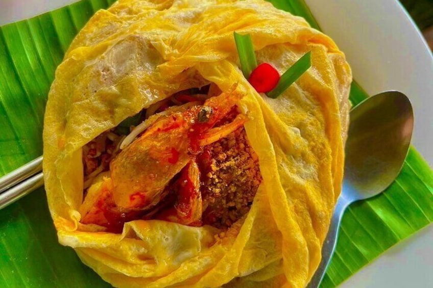 Un plato envuelto en hojas amarillas, adornado con chile rojo y cebollines, servido sobre una hoja de plátano. 1