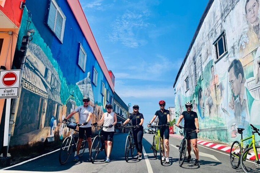 A group of cyclists on a street with colorful murals on the buildings. 1