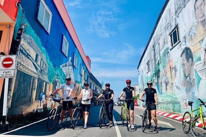 A group of cyclists on a street with colorful murals on the buildings. 1