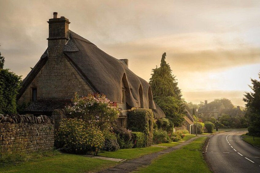 A stone house with a thatched roof, surrounded by lush greenery and a winding road. 2