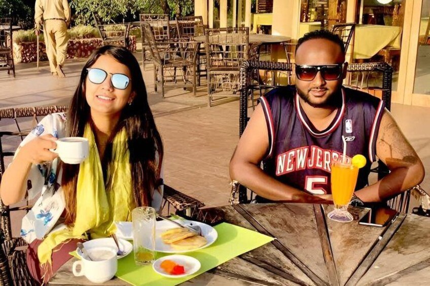Two people sitting at an outdoor cafe with a table set for a meal, including a drink and bread. 4