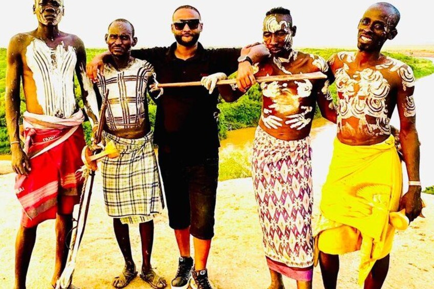Five men standing outdoors, some wearing traditional attire with patterns and designs. 2