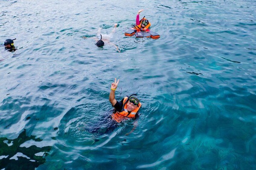 A person swimming in clear blue water, wearing an orange life jacket. 2