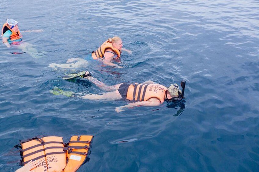 Three people swimming in the ocean, each wearing a life jacket. 5