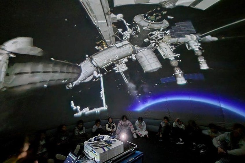 Une navette spatiale se trouve dans un hangar, et un groupe de personnes l’observe. 1