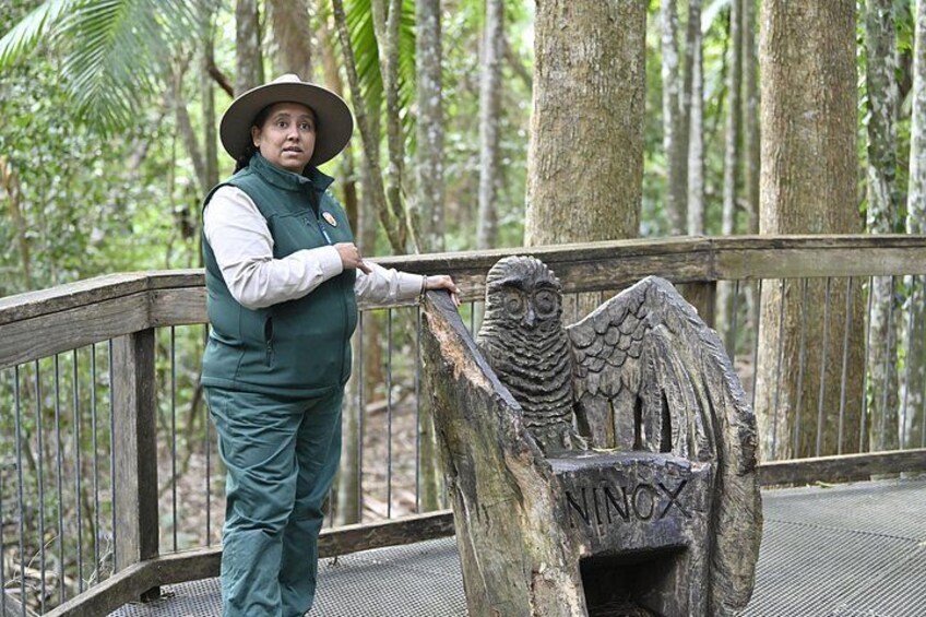 A person in a green uniform and hat standing on a wooden bridge with a carved owl sculpture. 3