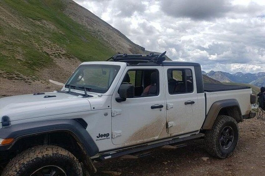 A white Jeep with off-road tires parked on a dirt path with mountains in the background. 4