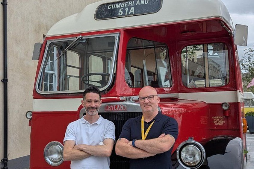 Dos hombres de pie frente a un autobús antiguo rojo y blanco con el número 51A y la palabra 'CUMBERLAND' visible en la parte delantera. 4
