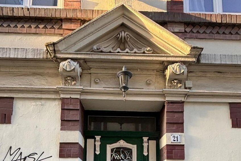 A building facade with a decorative entrance, a street lamp, and a number plaque. 2