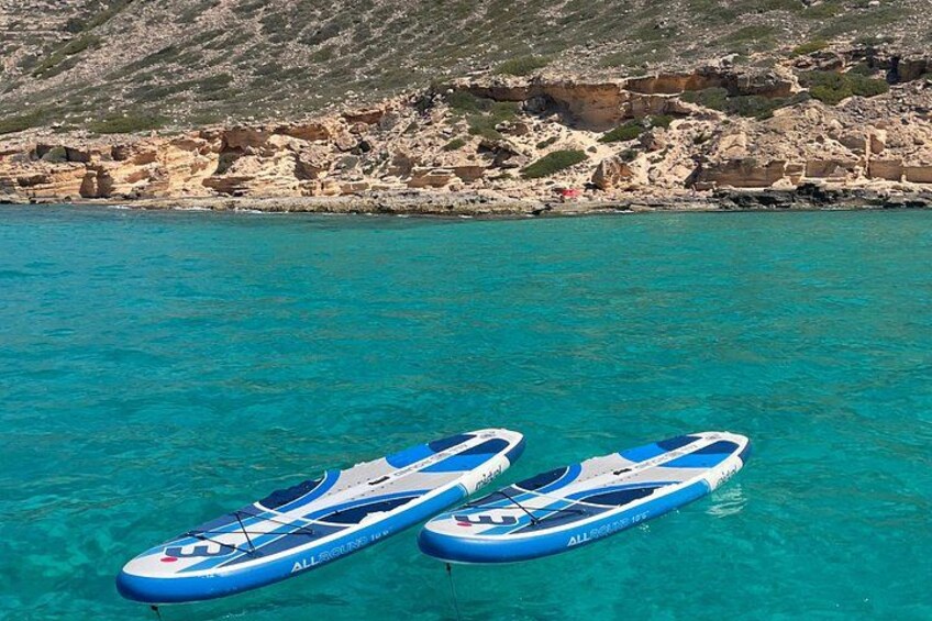 Twee blauwe paddleboards drijven op turquoise water, met rotsachtige kliffen op de achtergrond. 4