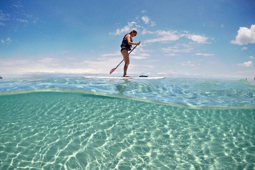 A person paddleboarding on clear turquoise water with a boat in the background. 3