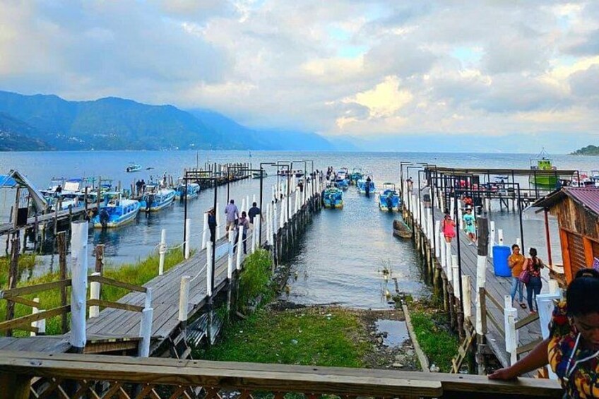 Eine Pier mit vertäuten Booten, ein hölzerner Steg und eine bergige Landschaft im Hintergrund. 1