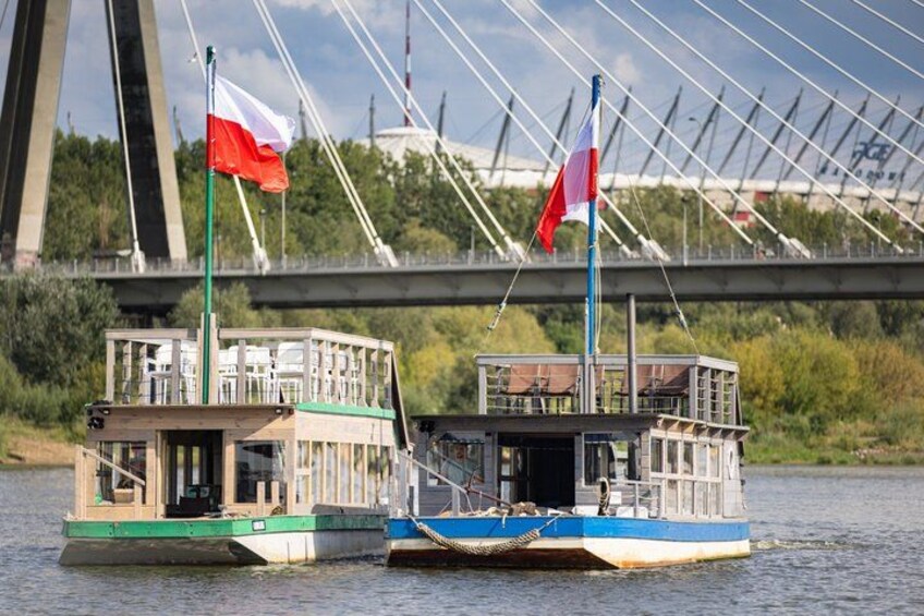 Deux péniches, ornées de drapeaux, flottent sur une rivière, avec un pont en arrière-plan. 3