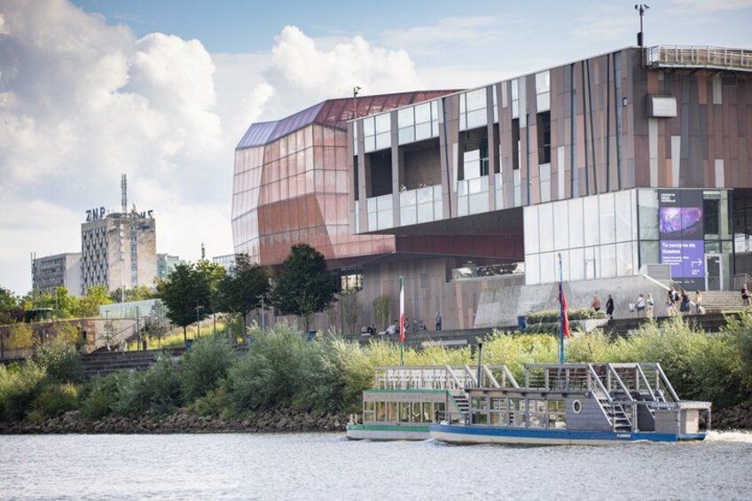 Un bâtiment moderne à la façade de verre, avec une rivière et un bateau amarré au premier plan. 1
