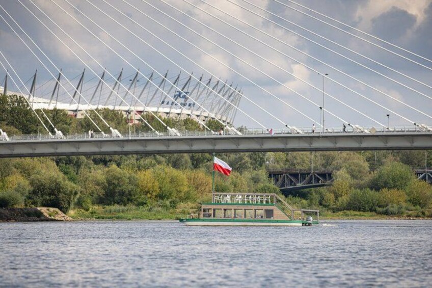 Un pont à câbles, un bateau arborant un drapeau et de la végétation le long de la rive. 2