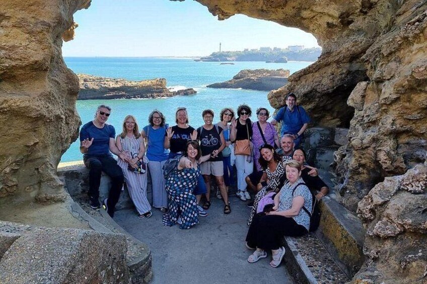 A group of people posing in front of a natural rock formation with a coastal view. 1