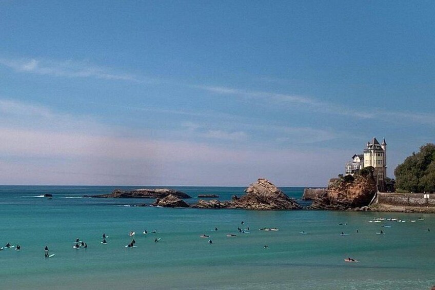 A coastal scene with clear water, a castle-like structure, and several people swimming. 4