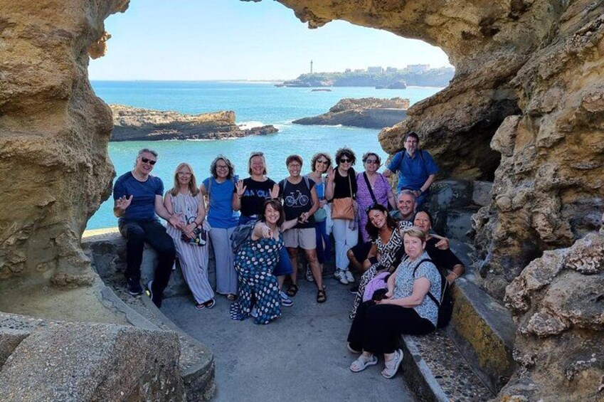 A group of people posing in a rocky archway with a coastal view. 1