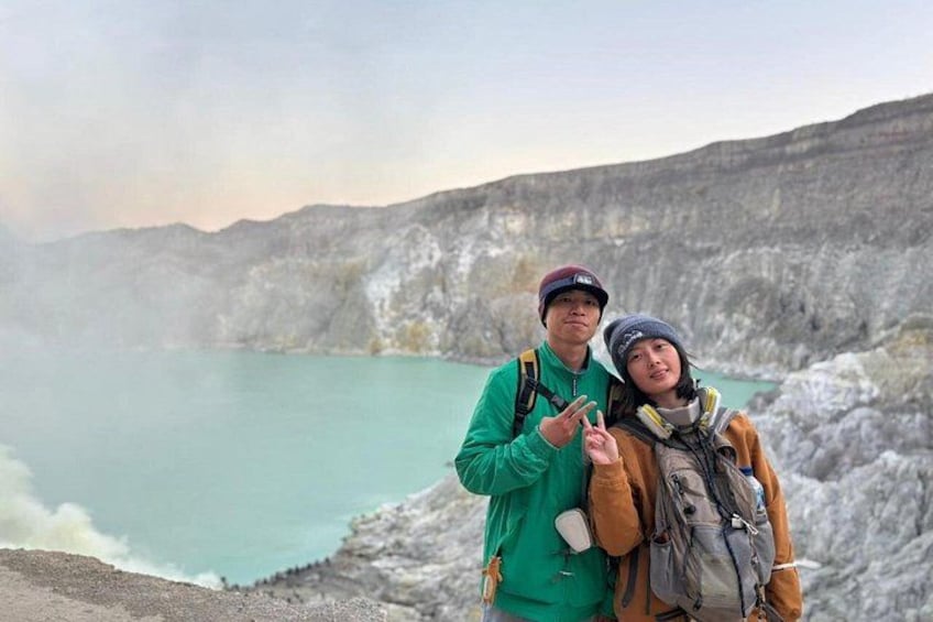 Dos personas de pie junto a un lago turquesa con un paisaje rocoso al fondo. 1
