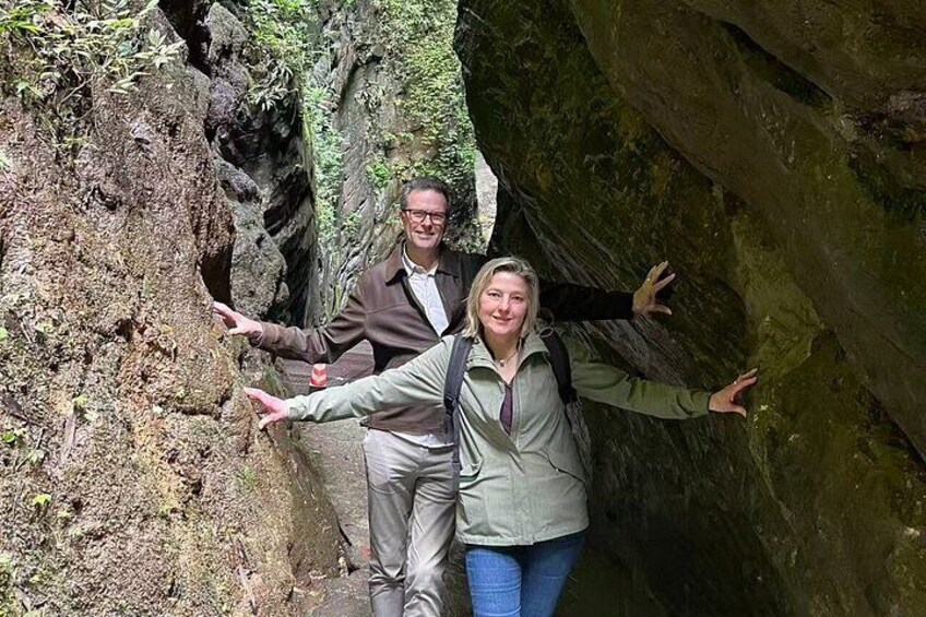 Two people standing in a narrow canyon with rocky walls and sparse vegetation. 2