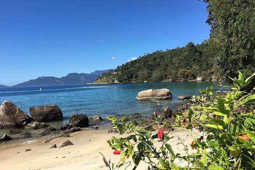 Una playa con grandes rocas, agua azul cristalina y un promontorio boscoso. 2