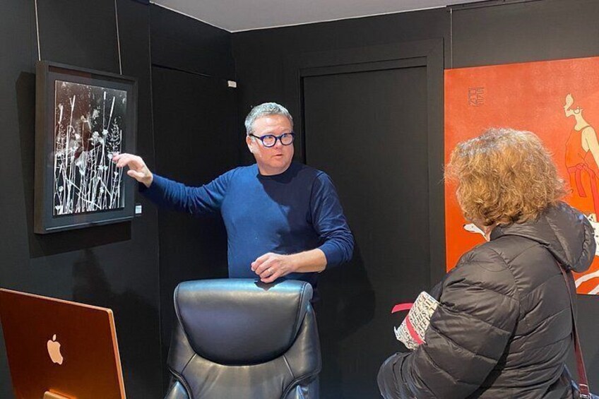 Una persona indica un quadro appeso al muro, un'altra è seduta su una sedia e un laptop è appoggiato su un tavolo. 3