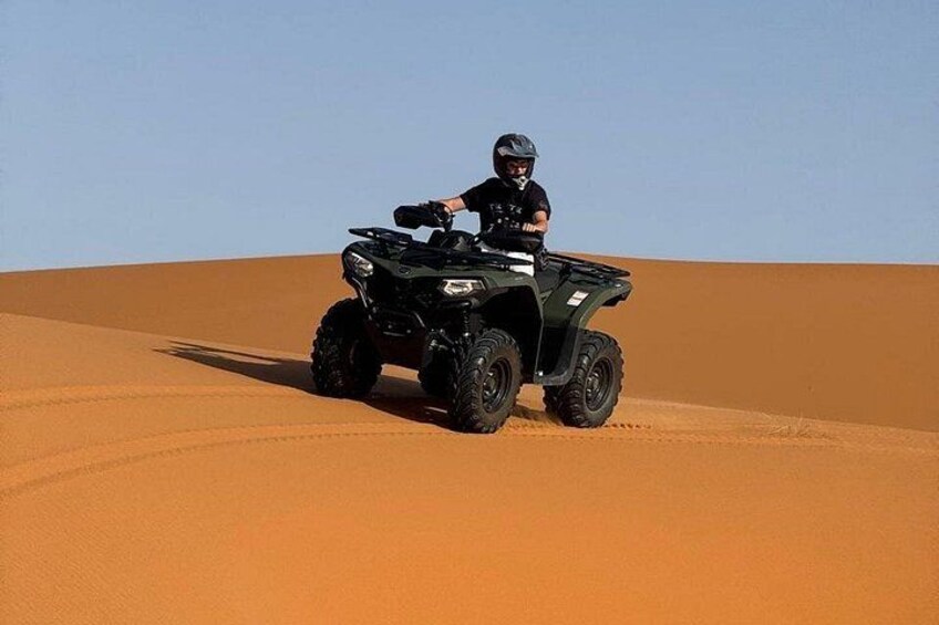 Een persoon rijdt op een quad over een zandduin. 1