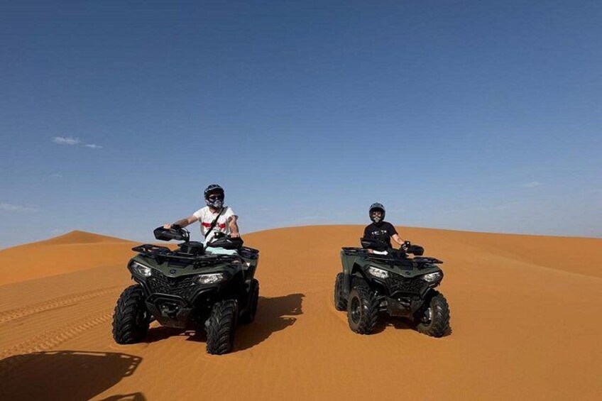 Twee personen rijden op quadbikes over een zandduin in de woestijn. 4