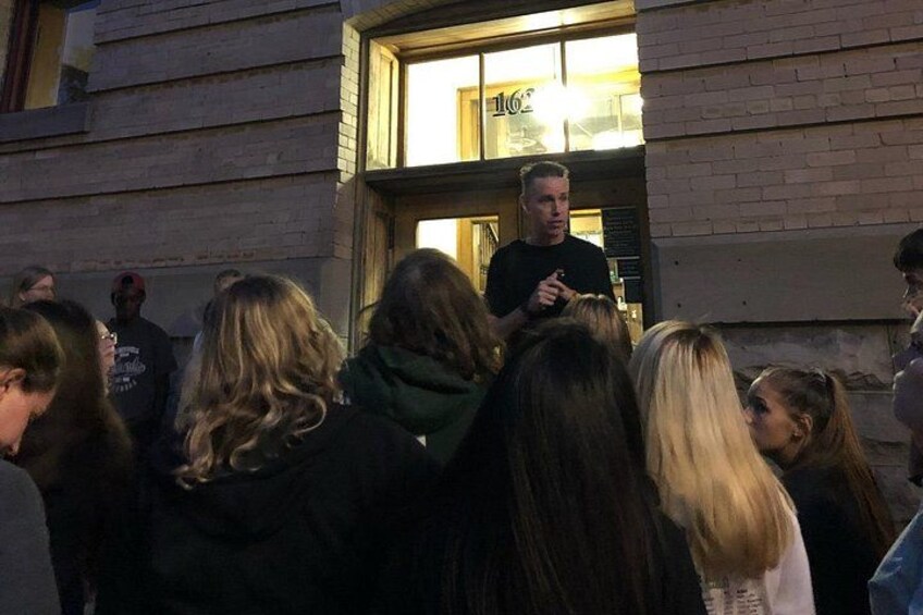 Eine Gruppe von Menschen hat sich vor einem Gebäude versammelt, an dem ein Schild mit der Aufschrift '162' angebracht ist. 5