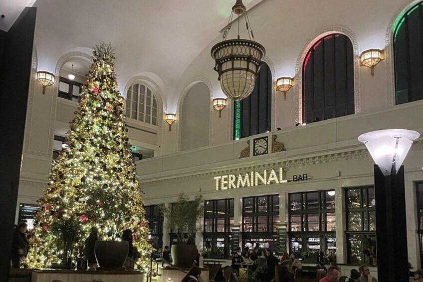 Ein großer Weihnachtsbaum in einer Lobby, im Hintergrund eine Bar namens 'Terminal Bar'. 4