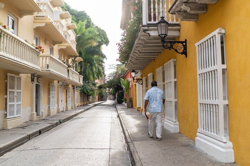 Una calle estrecha bordeada de edificios amarillos, una persona caminando y un farol. 4