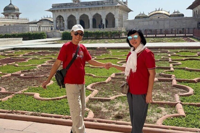 Due persone con camicie rosse in un giardino caratterizzato da motivi geometrici, con un grande edificio con cupole sullo sfondo. 4