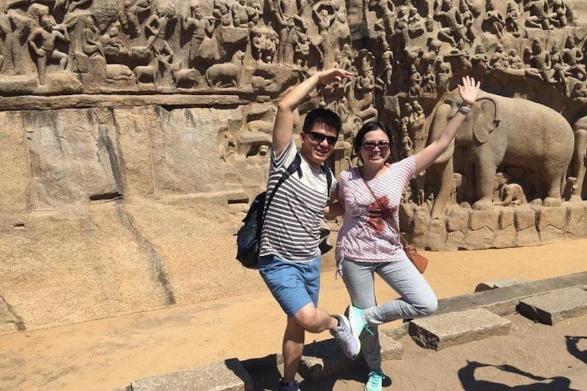 Deux personnes posent devant une grande sculpture en pierre représentant des éléphants et des figures humaines. 2