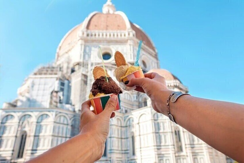 Deux mains tenant des cornets de glace devant un grand bâtiment à coupole. 2