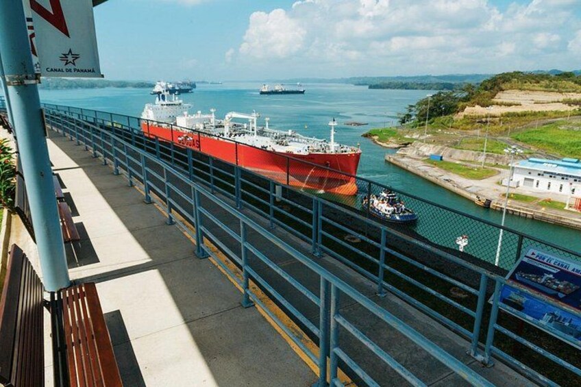 Un barco rojo grande atracado en un puerto con una lancha de remolque más pequeña cerca, una barandilla azul y un cielo despejado. 2