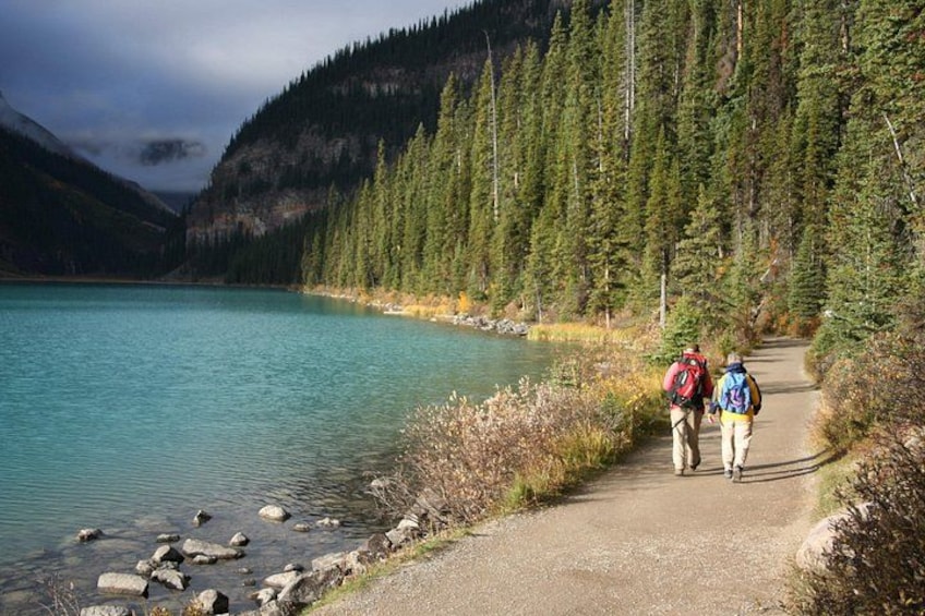 A hiking trail beside a lake with dense forest and mountains in the background. 1