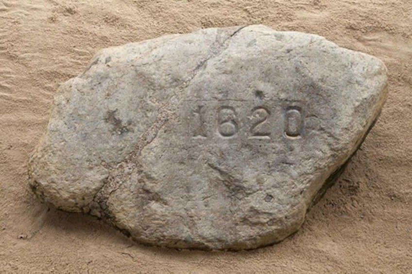 A large, weathered stone with the number '1820' engraved on it, set against a sandy background. 1