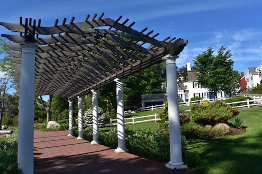 A wooden pergola with white columns, a brick pathway, and a white fence in a garden setting. 2