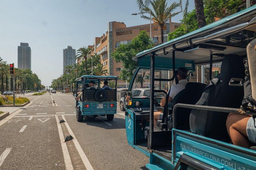 A blue bus with passengers, a blue jeep, and palm trees on a city street. 1