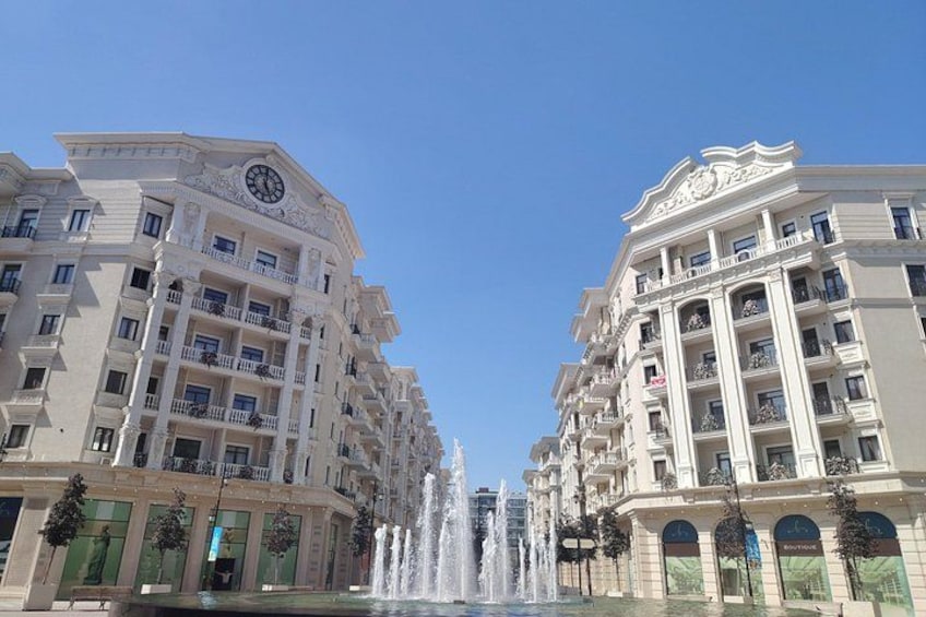 Un edificio grande con un reloj, una fuente y otro edificio con balcones. 3