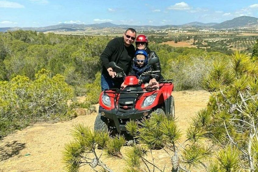 Een man en een kind op een rode quad in een woestijnlandschap met schaarse begroeiing en verre bergen. 5