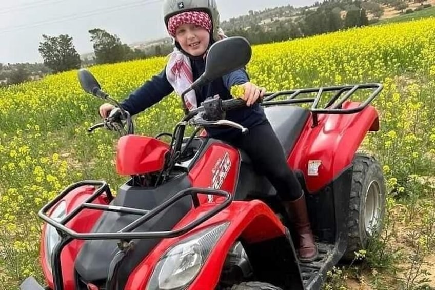 Een persoon op een rode quad rijdt door een veld vol gele bloemen. 3