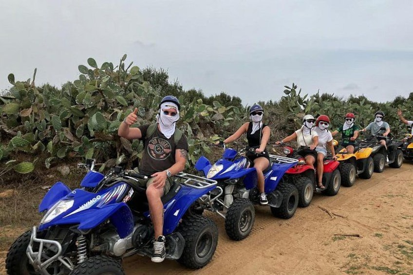 Een groep mensen rijdt op quads over een onverhard pad, met cactussen op de achtergrond. 1