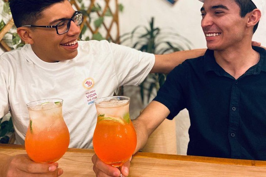 Two people holding glasses of a beverage, one wearing a white shirt and the other in a dark shirt, with a wooden table in front of them. 5